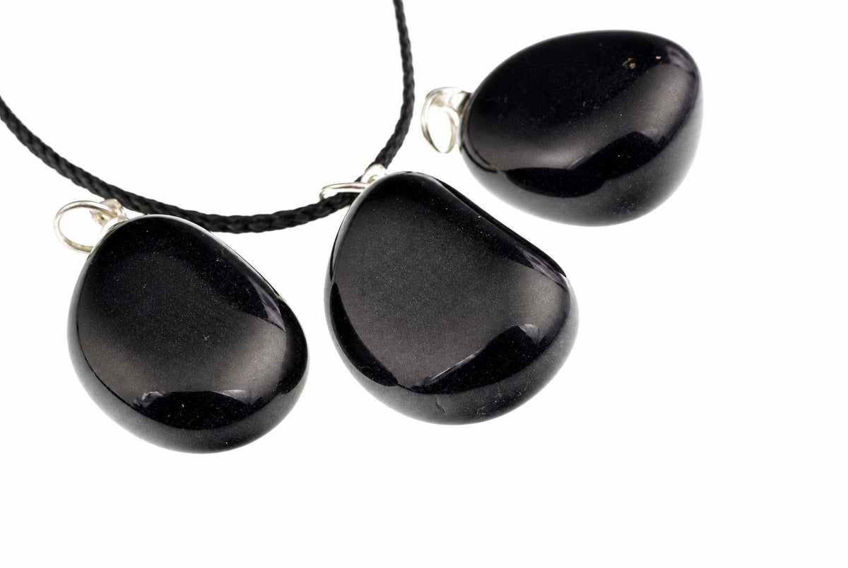 Three smooth black onyx pendants have rounded pebble shapes and reflective surfaces, with silver-colored loops and a black cord on white.
