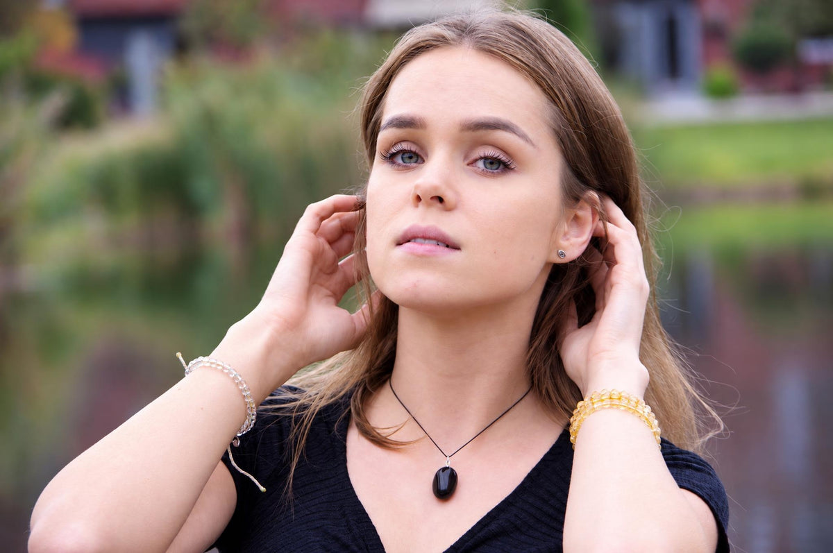 A woman wears a black onyx pendant on a thin cord, with clear and yellow beaded bracelets on her wrists.