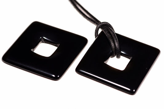 Two glossy black square pendants with rounded corners and a central square cutout, one attached to a dark cord on a white surface.
