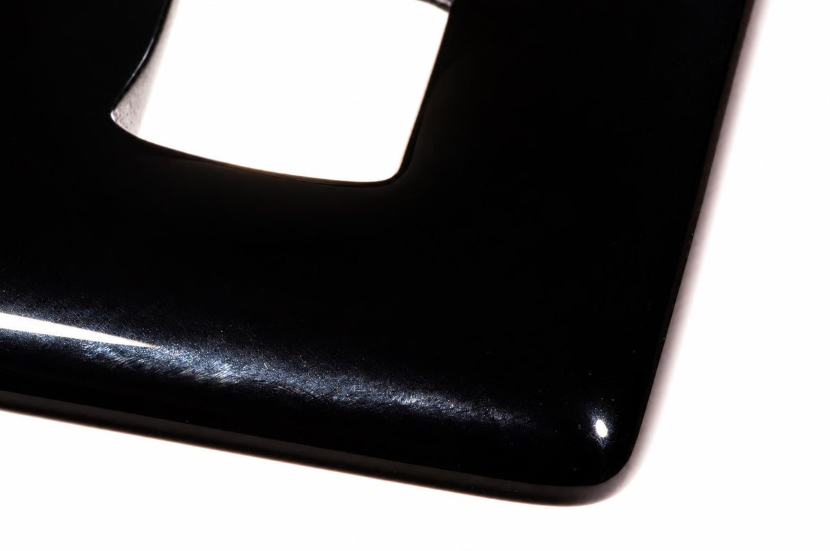 A close-up of a glossy black pendant with a square cutout, resting on a white surface.