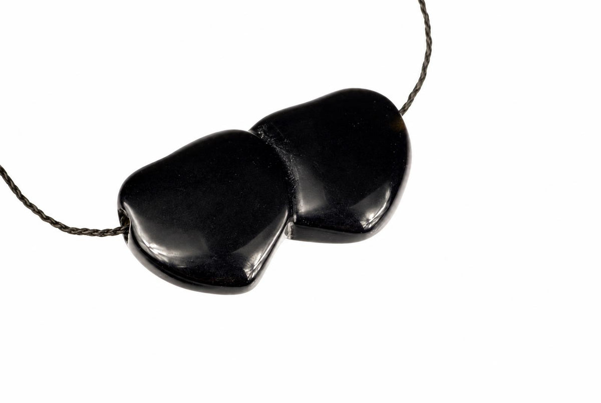 A black pendant with two smooth, heart-shaped stones joined together on a dark cord against a white background.