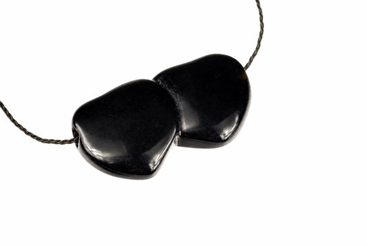 A black pendant with two smooth, heart-shaped stones joined together on a dark cord against a white background.