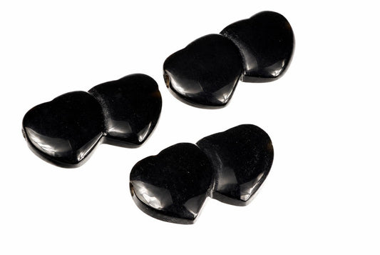 Three black, polished heart-shaped beads with a glossy finish are arranged on a white surface.