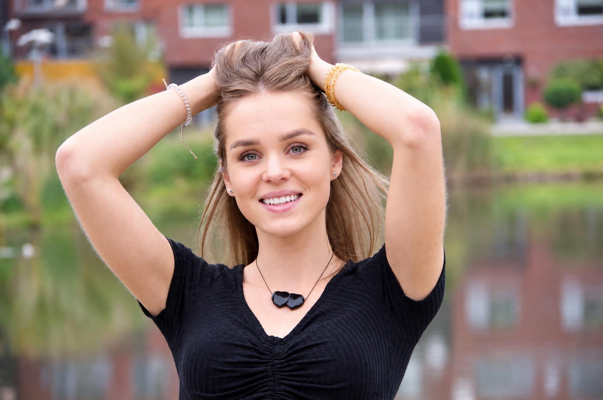 A woman wears a black top and a necklace with two dark, heart-shaped pendants on a thin cord.