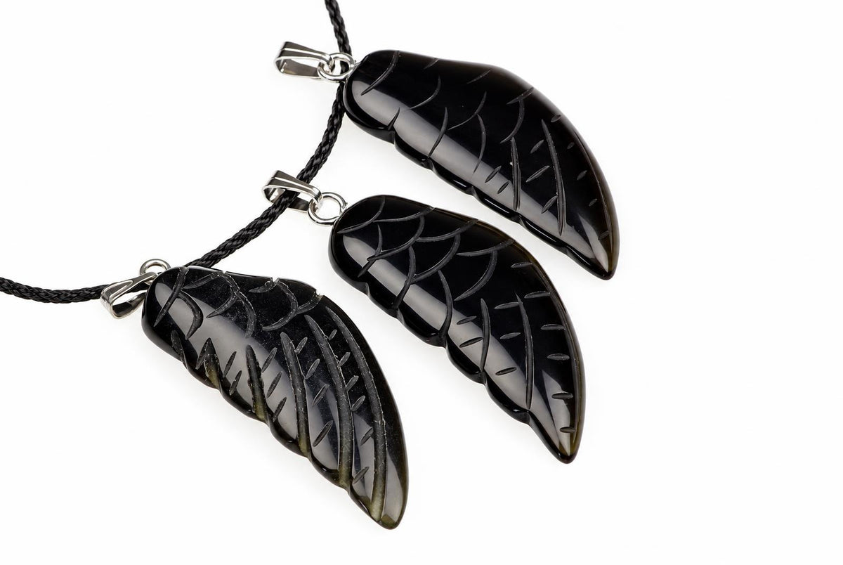 Three black onyx pendants shaped like wings, each with carved vein details and a silver-toned bail on a dark cord against a white background.