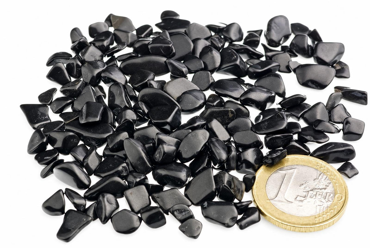 A pile of small, smooth black stones on a white surface with a one euro coin for scale.