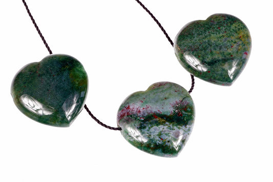 Three polished heart-shaped beads in green, red and white tones on a dark cord against a white background.