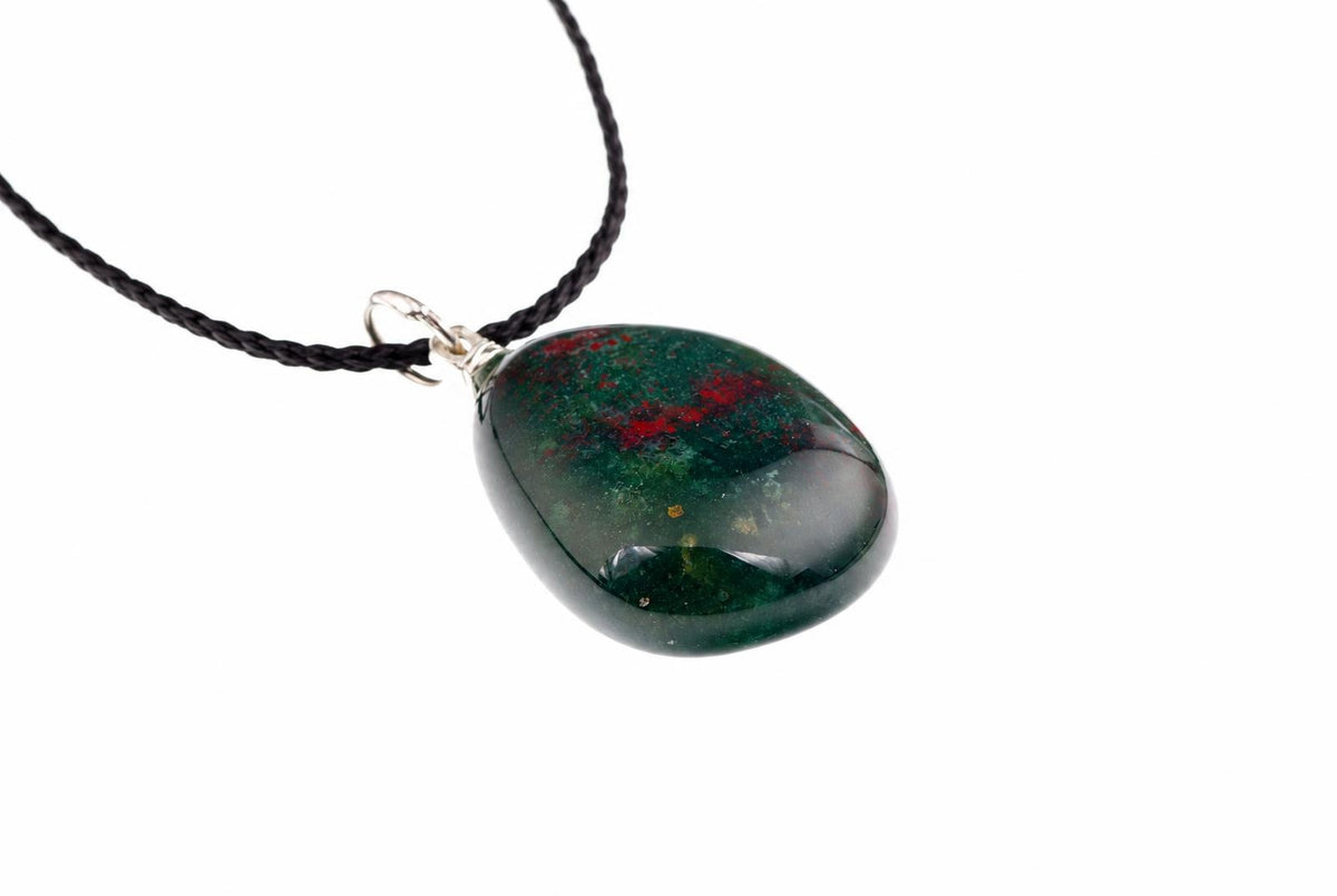 A polished pebble-shaped pendant with dark green and red inclusions hangs from a black cord against a white background.