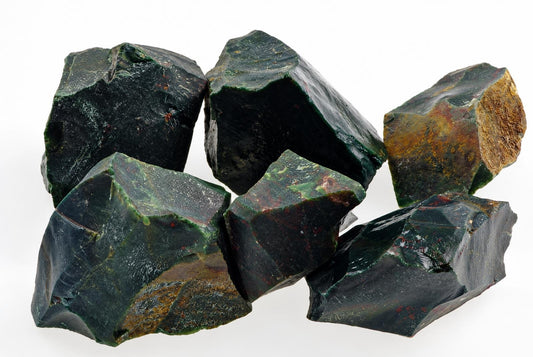Six raw bloodstone pieces with dark green, black and brown surfaces on a white background.