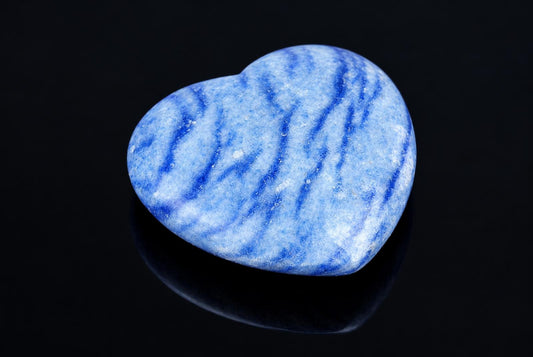 A polished heart-shaped stone with blue and white wavy stripes on a dark, reflective surface.