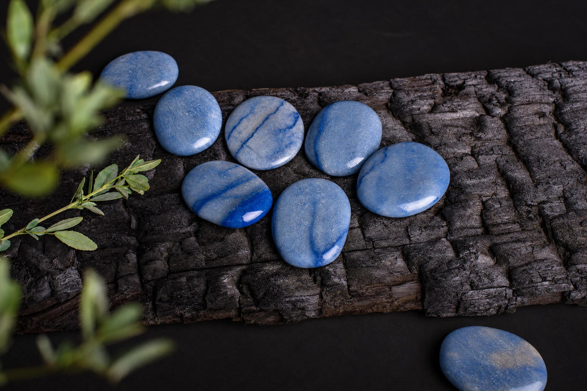 Several smooth, blue quartz palmstones with white and dark blue veining rest on a dark wooden surface.