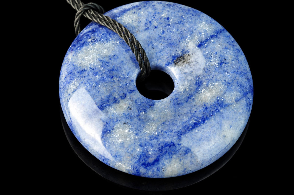 A polished blue and white quartz pendant shaped like a donut with a central hole, threaded on a dark cord against a black background.
