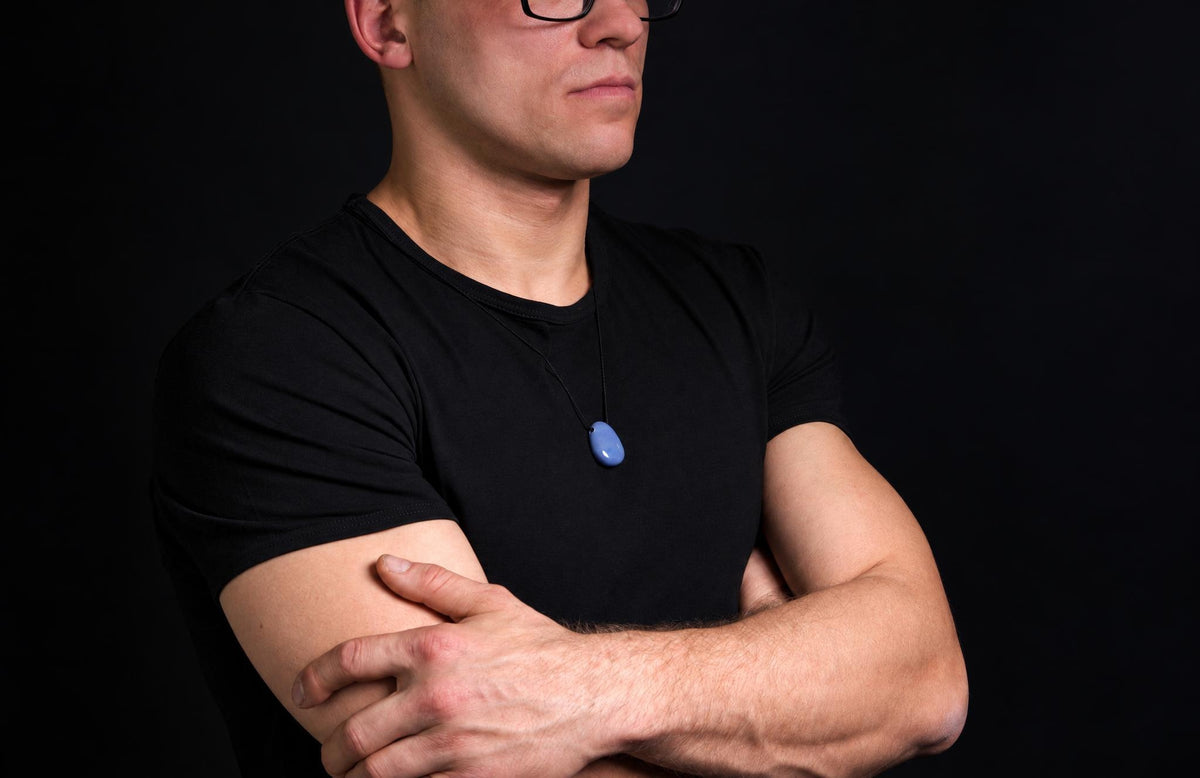 A man in a black t-shirt wears a blue pendant on a dark surface.