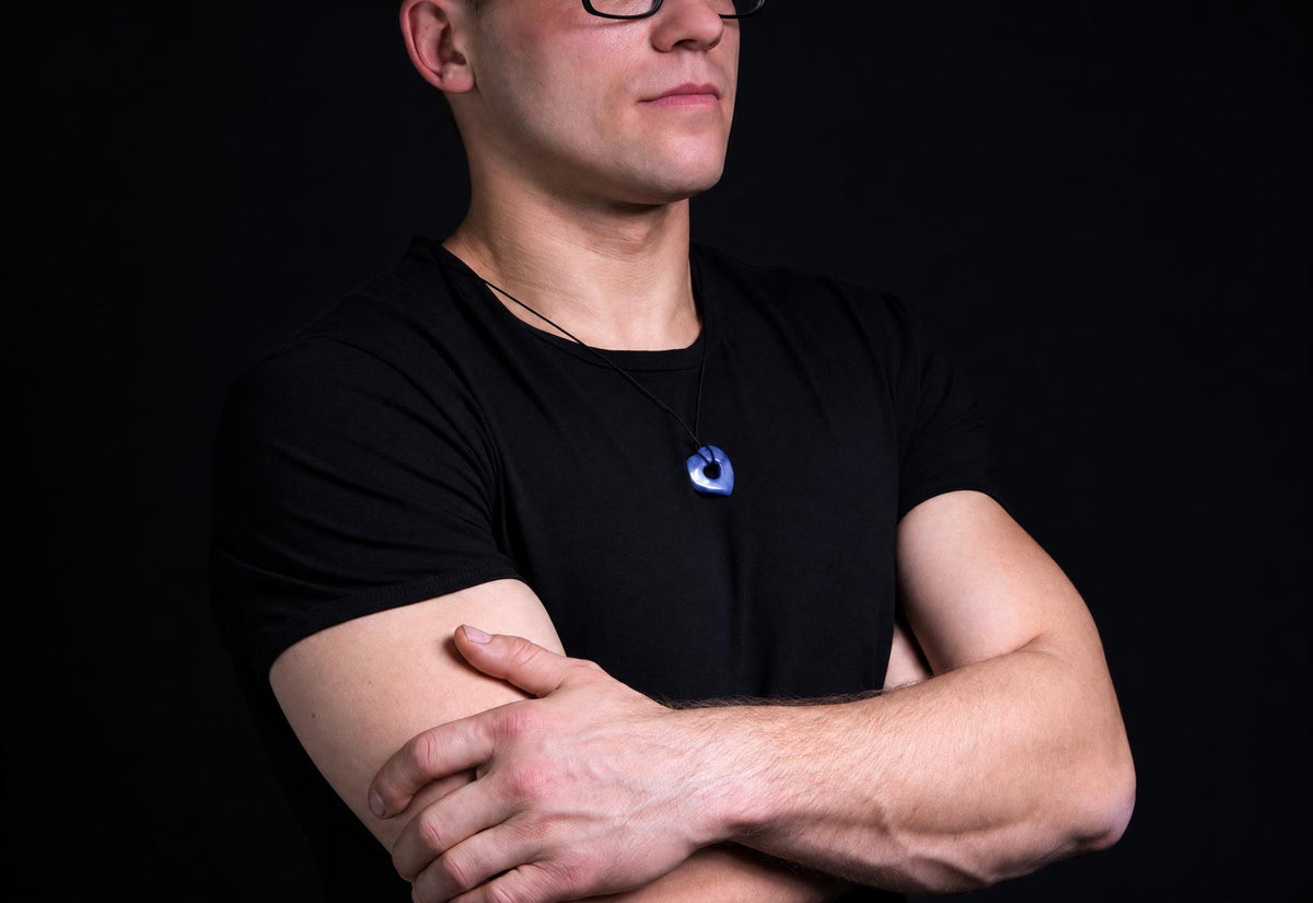 A man in a black t-shirt wears a blue pendant on a dark surface.