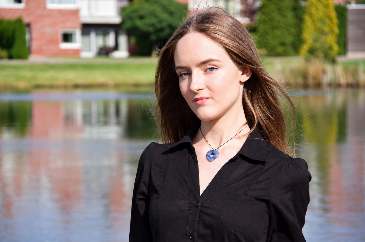 A woman wears a black shirt and a necklace with a blue, heart-shaped pendant on a dark cord.