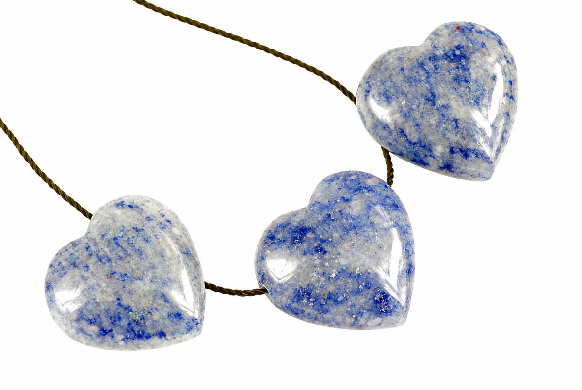 Three polished heart-shaped blue quartz pendants on a dark cord against a white background.