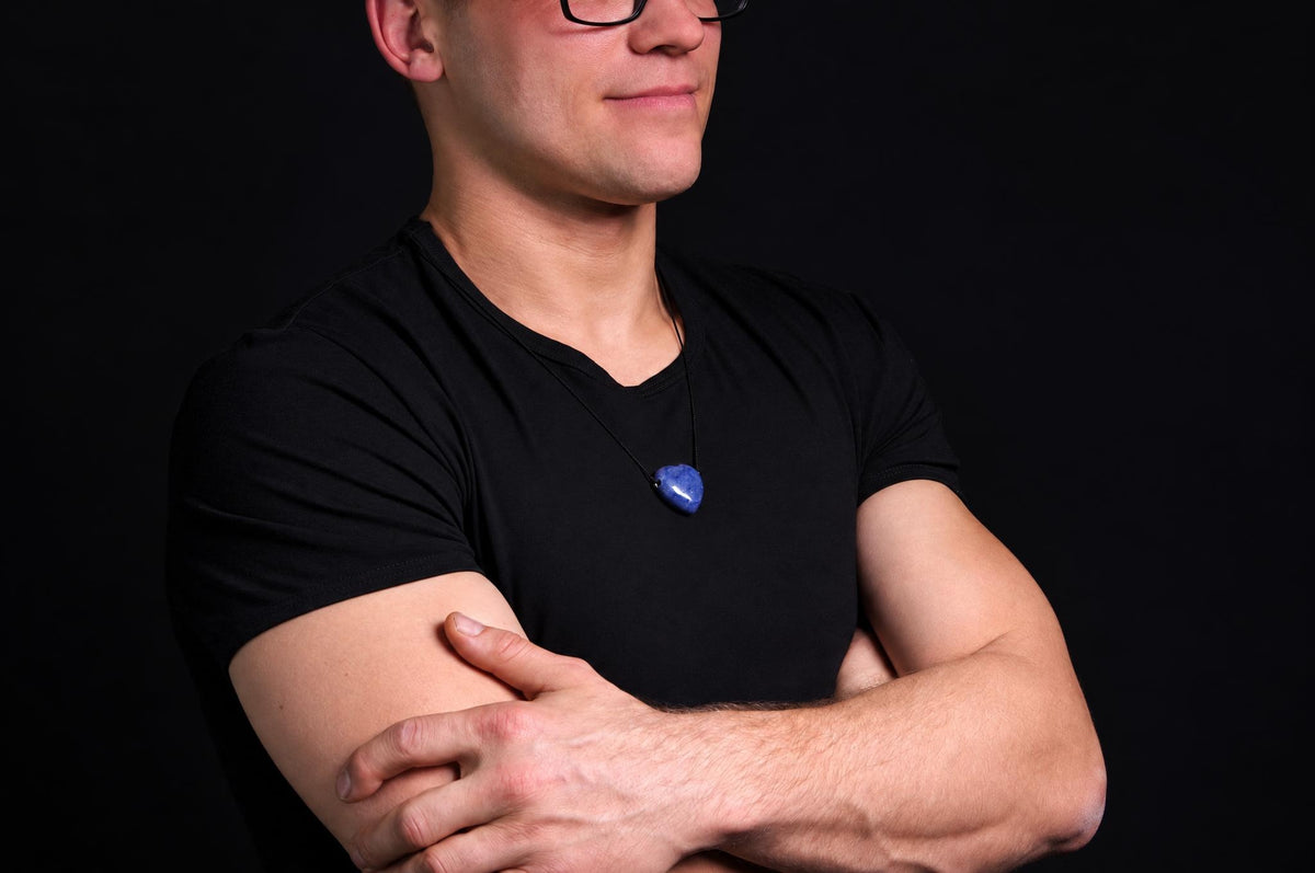 A man in a black t-shirt wears a blue pendant on a dark surface.
