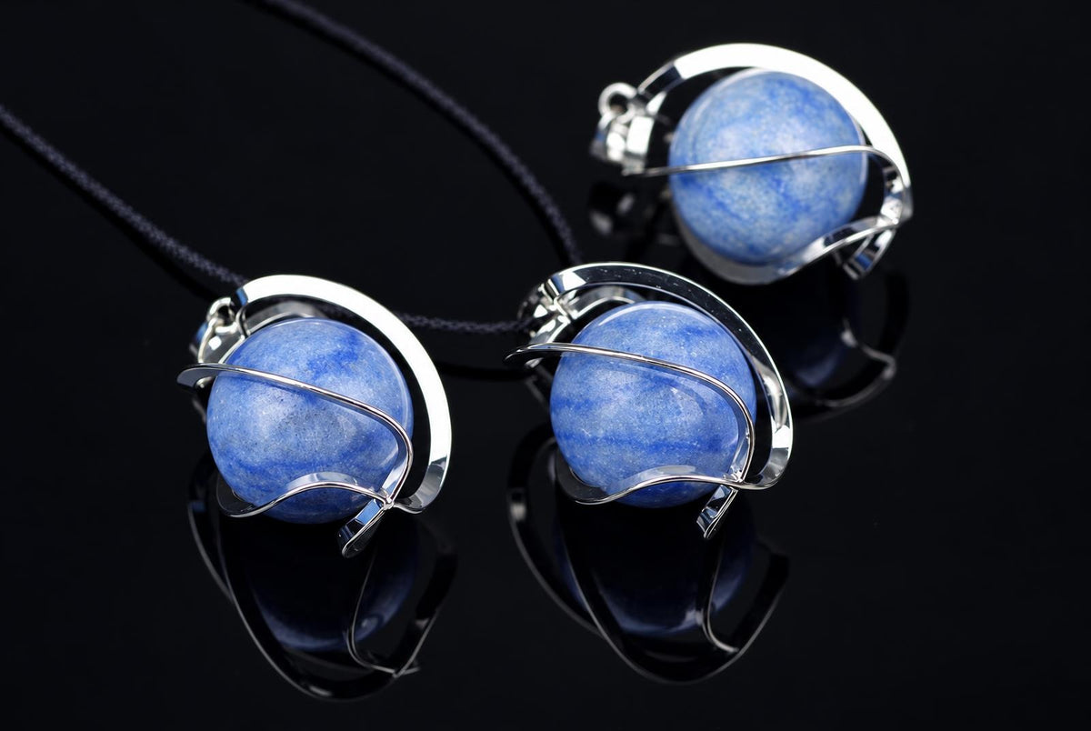 Three blue quartz spheres in silver-toned wire settings on a dark reflective surface.