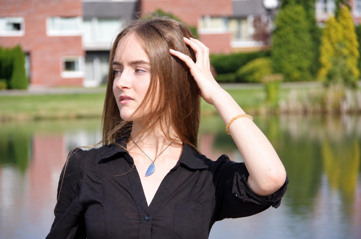A woman wears a black shirt and a blue pendant on a thin cord, with a yellow beaded bracelet on her wrist.