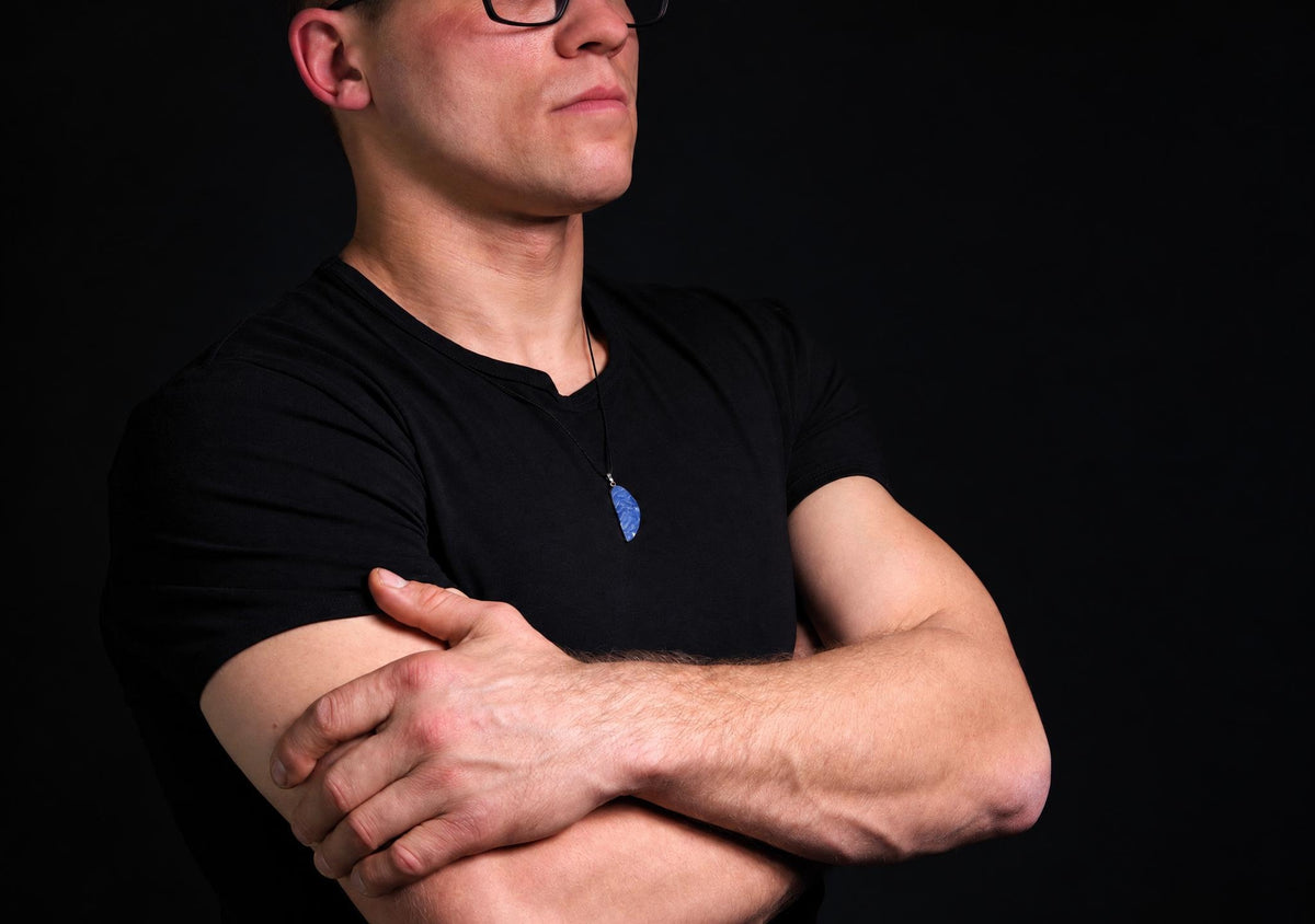 A man in a black t-shirt wears a blue pendant on a dark surface.