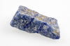 A rough, irregular piece of blue quartz with white and gold-coloured patches on a pale surface.