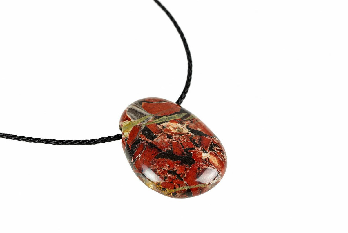 A polished oval pendant with red, black and green brecciated jasper on a black cord against white.