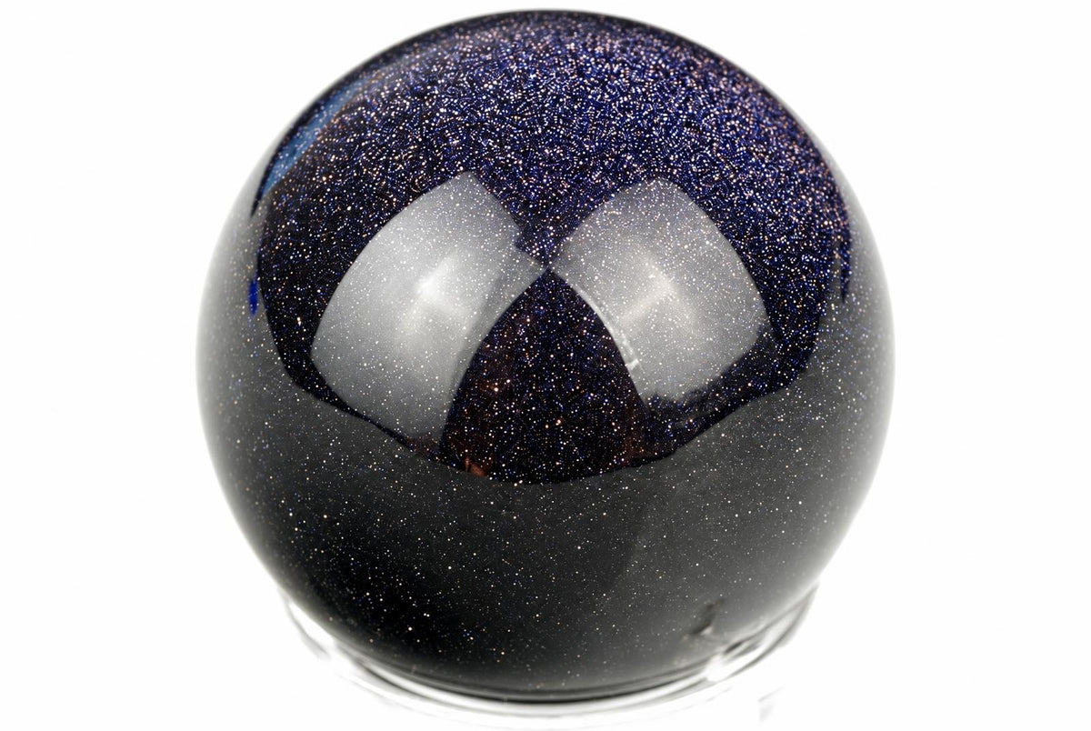 A dark, glittering sphere with a blue upper section and white reflections sits on a clear base against a white background.