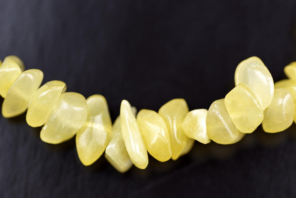 A strand of pale yellow, polished calcite chips arranged in a loose curve on a dark surface.