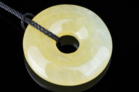 A yellow and white polished donut-shaped pendant with a central hole, attached to a dark cord against a black surface.