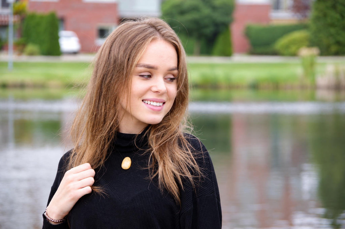 A woman wears a black turtleneck with a smooth, oval-shaped gold-coloured pendant at the neckline.