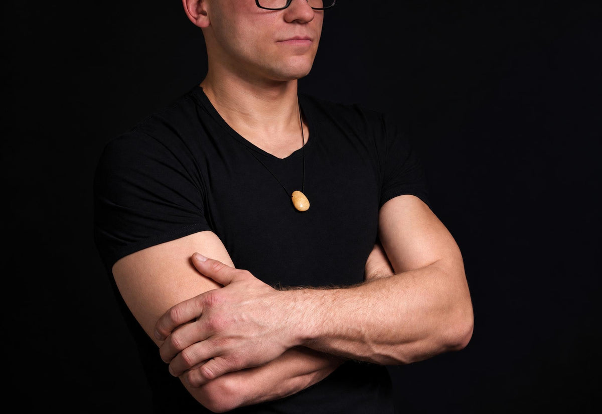 A man in a black shirt wears a necklace with a smooth, pale yellow drop-shaped pendant against a dark background.