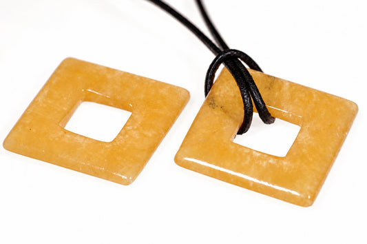 Two square, yellow-orange calcite pendants with central holes lie on a white surface; one has a black cord threaded through its hole.