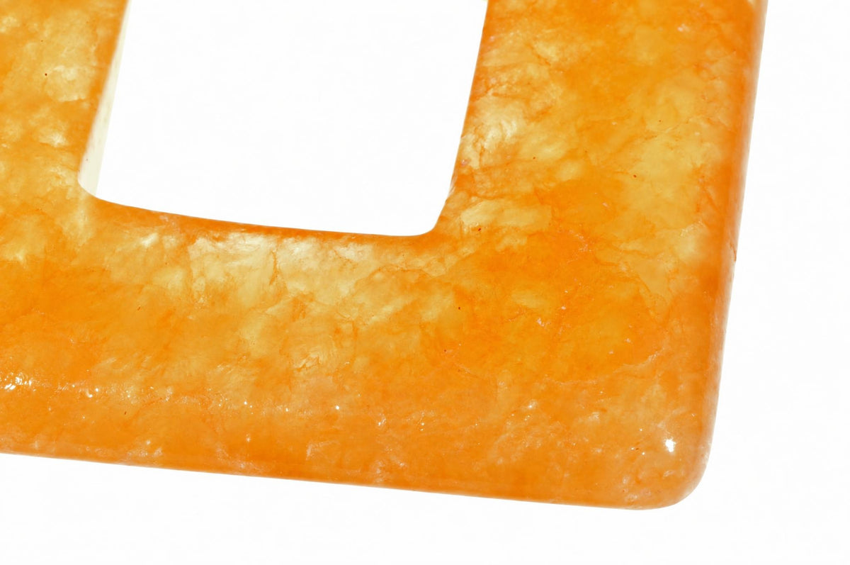 A close-up of a square, orange-yellow calcite pendant with a central cutout, showing its polished surface and rounded edges.