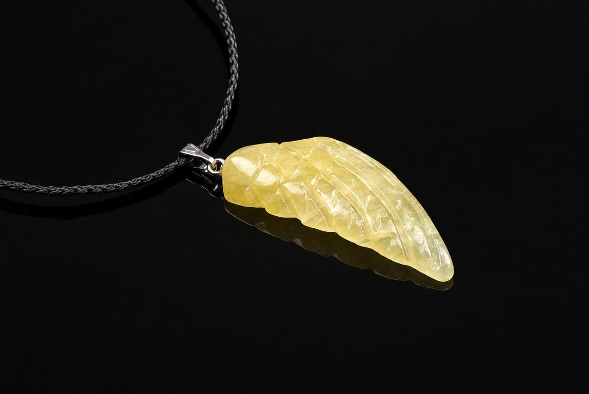 A pale yellow carved pendant shaped like a wing, attached to a dark cord on a black surface.