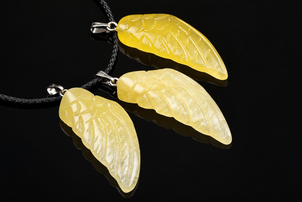 Three yellow calcite pendants shaped like wings, each with carved vein details, hanging from black cords on a dark surface.