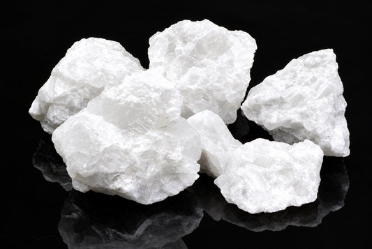 Several white calcite crystals with rough, jagged edges rest on a dark reflective surface.