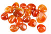 A collection of polished, smooth carnelian stones in shades of orange and red with white banding, arranged on a pale surface.