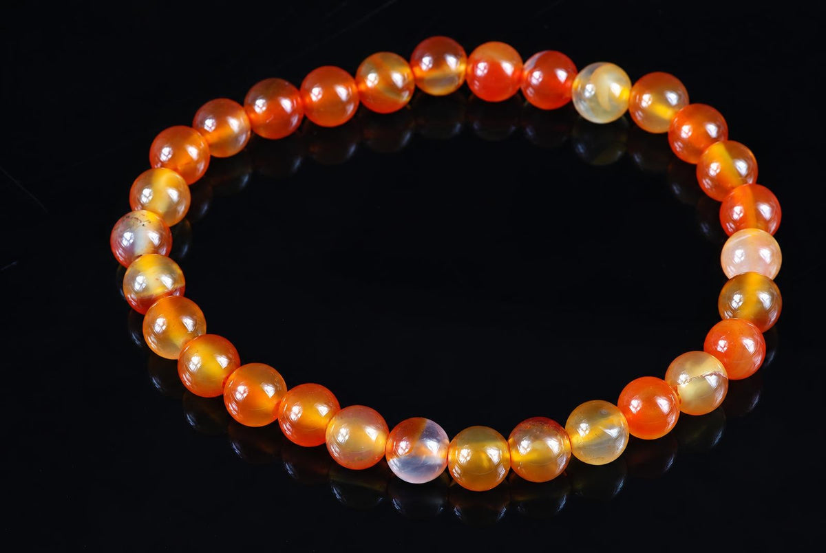 A bracelet of round beads in orange, yellow and pale tones arranged on a dark reflective surface.