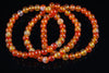 A coiled bracelet of round beads in orange, yellow and pale tones on a dark reflective surface.