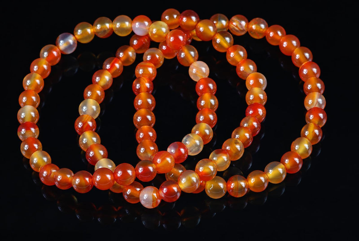 A coiled bracelet of round beads in orange, yellow and pale tones on a dark reflective surface.