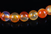 A row of round, polished beads in orange, yellow and pale purple tones on a dark surface.