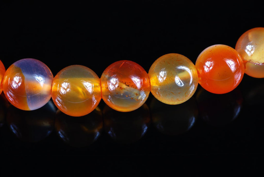 A row of round, polished beads in orange, yellow and pale purple tones on a dark surface.