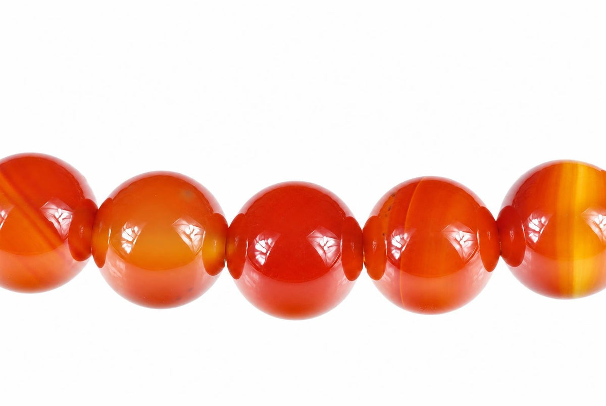 A row of round, polished beads in shades of orange and red on a pale surface.