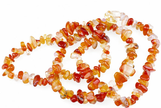 A necklace of irregular carnelian chips in red, orange, yellow and pale tones on a white surface.