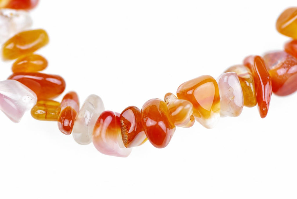Close-up of translucent orange, red and pale stone chips strung together against a white background.