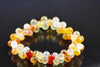 A bracelet of round beads in yellow, orange, white and red tones on a dark surface.