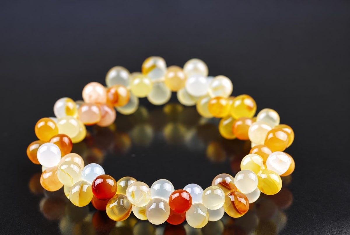 A bracelet of round beads in yellow, orange, white and red tones on a dark surface.