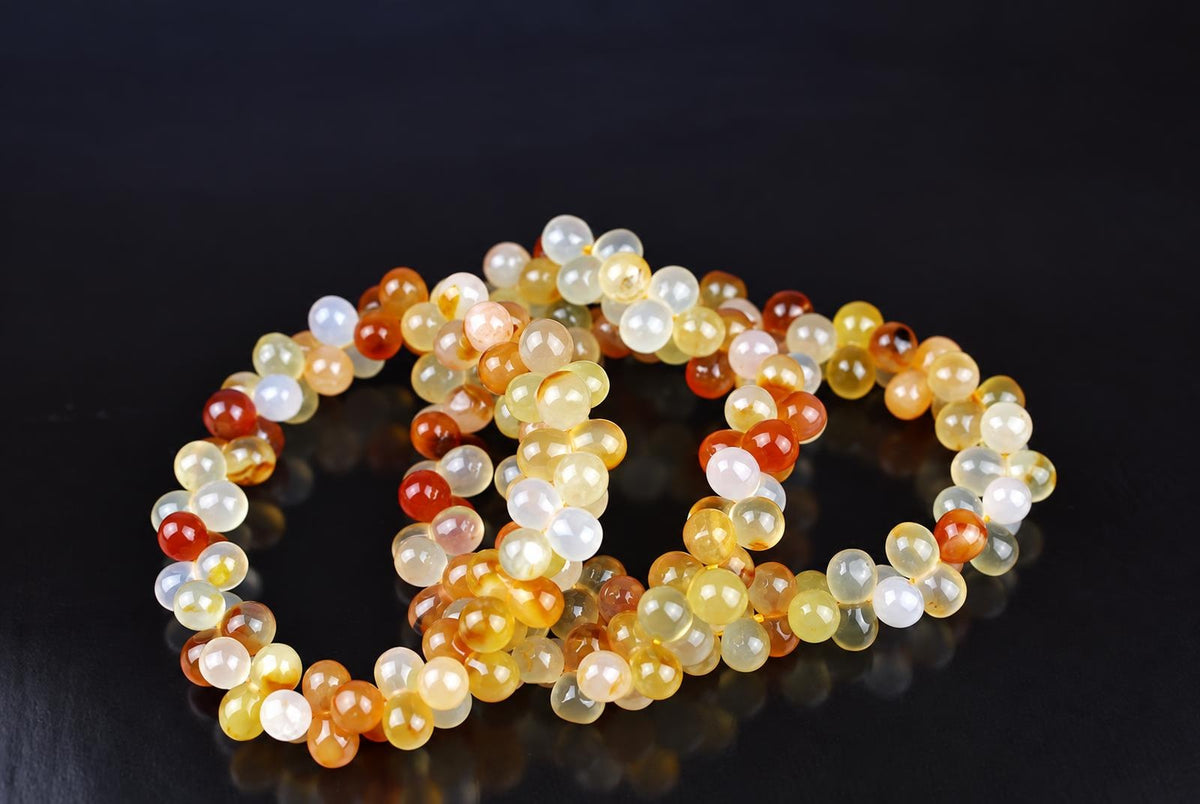A bracelet of round beads in yellow, orange, red and white tones on a dark surface.