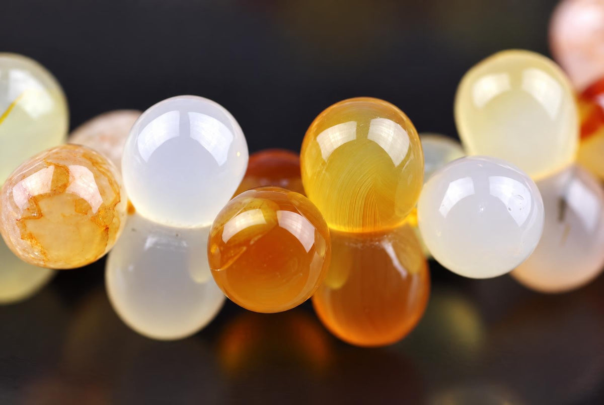 A close-up of a bracelet with round, polished beads in white, yellow, and orange tones on a dark surface.