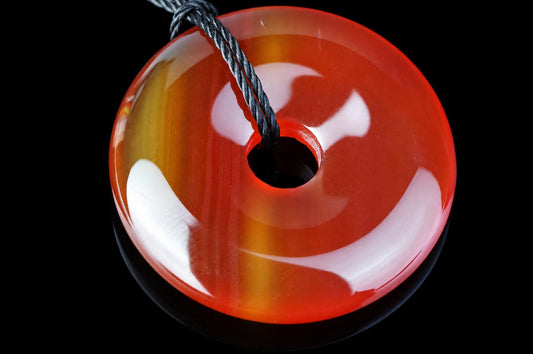 A polished, donut-shaped pendant with a central hole, featuring red, orange and yellow bands on a dark surface.